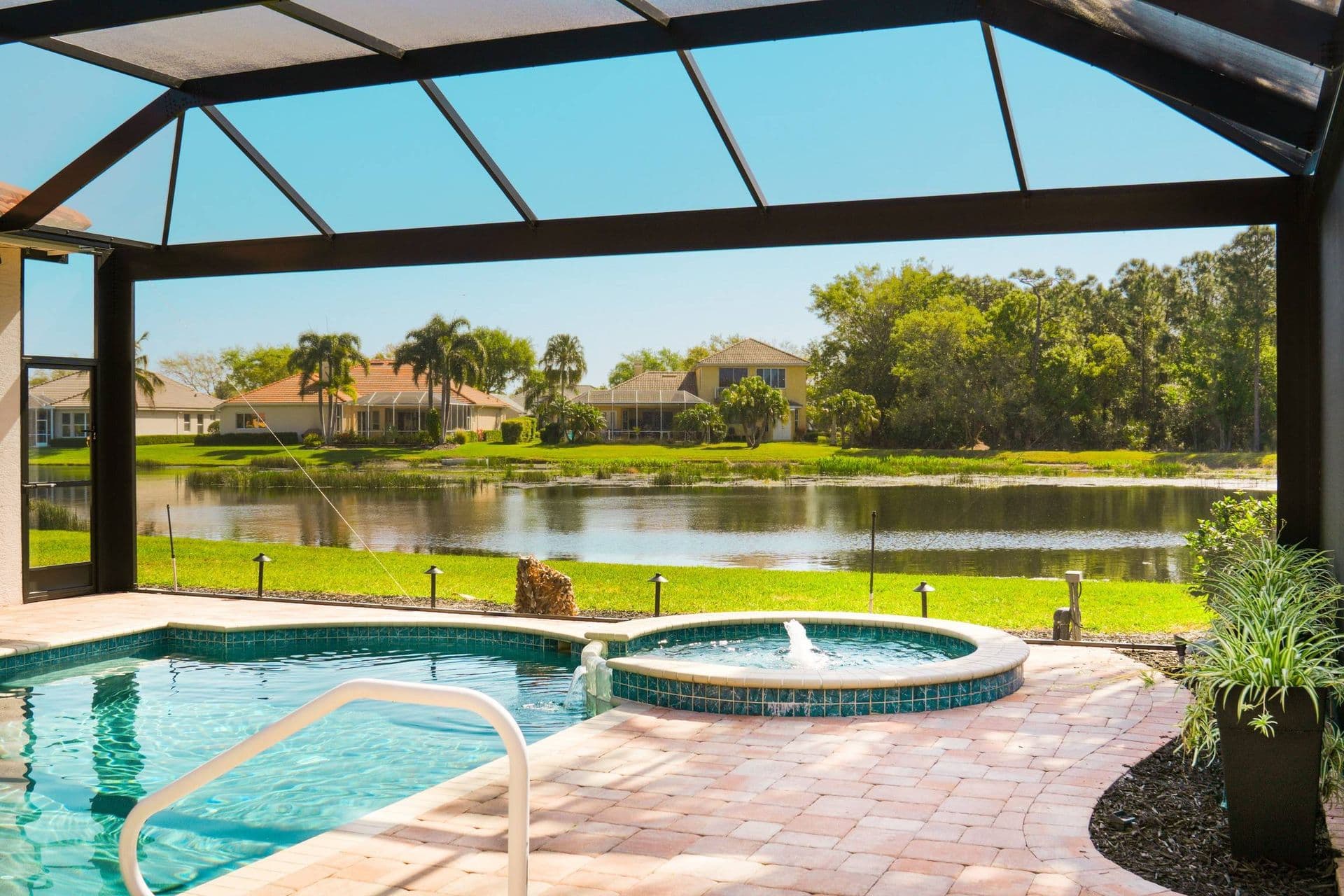 Screened lanai with pool and spa overlooking waterfront homes and lake with palm trees