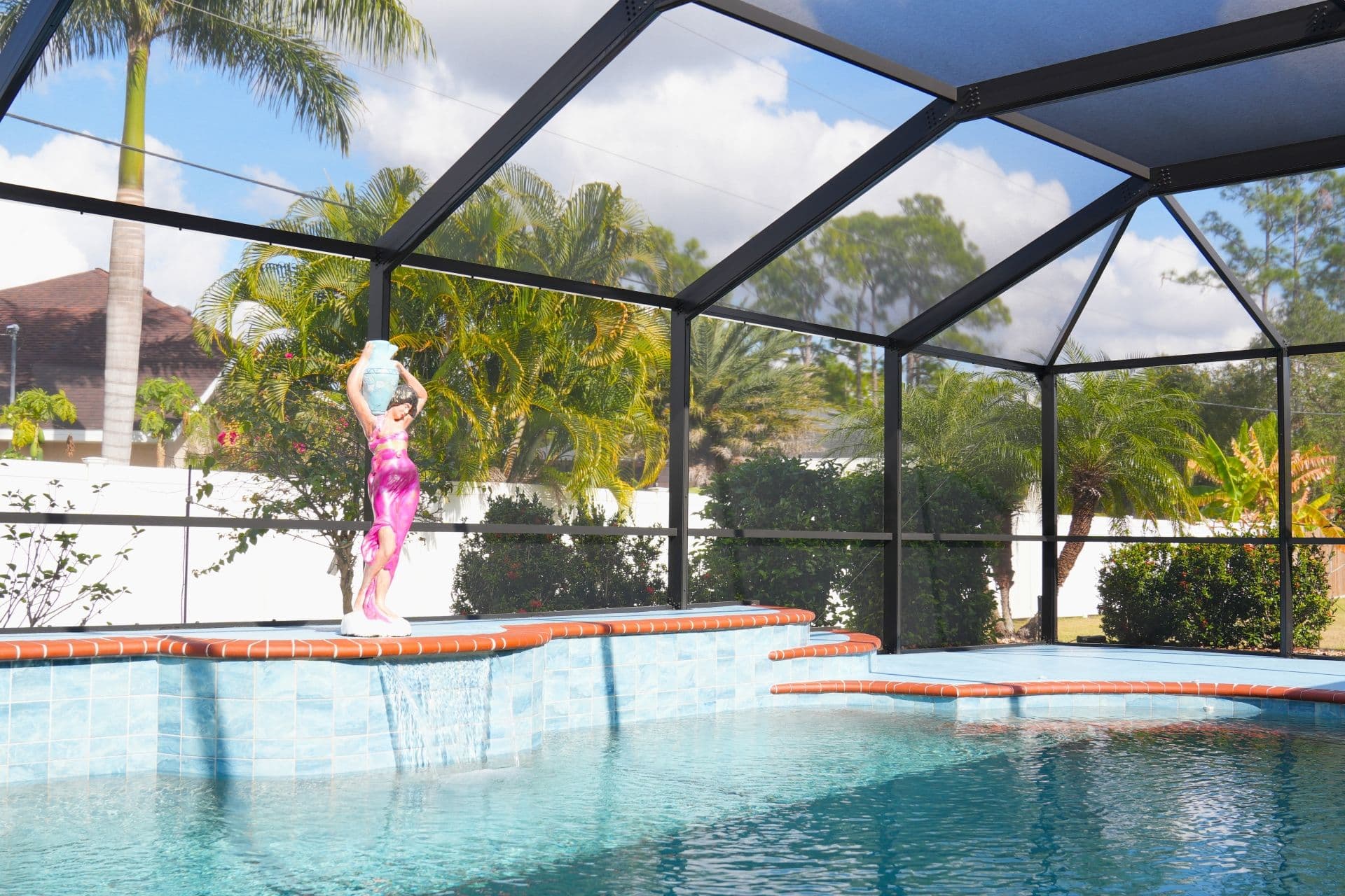 Sunny screened-in backyard pool with a statue at the edge, surrounded by palm trees under a bright blue sky.