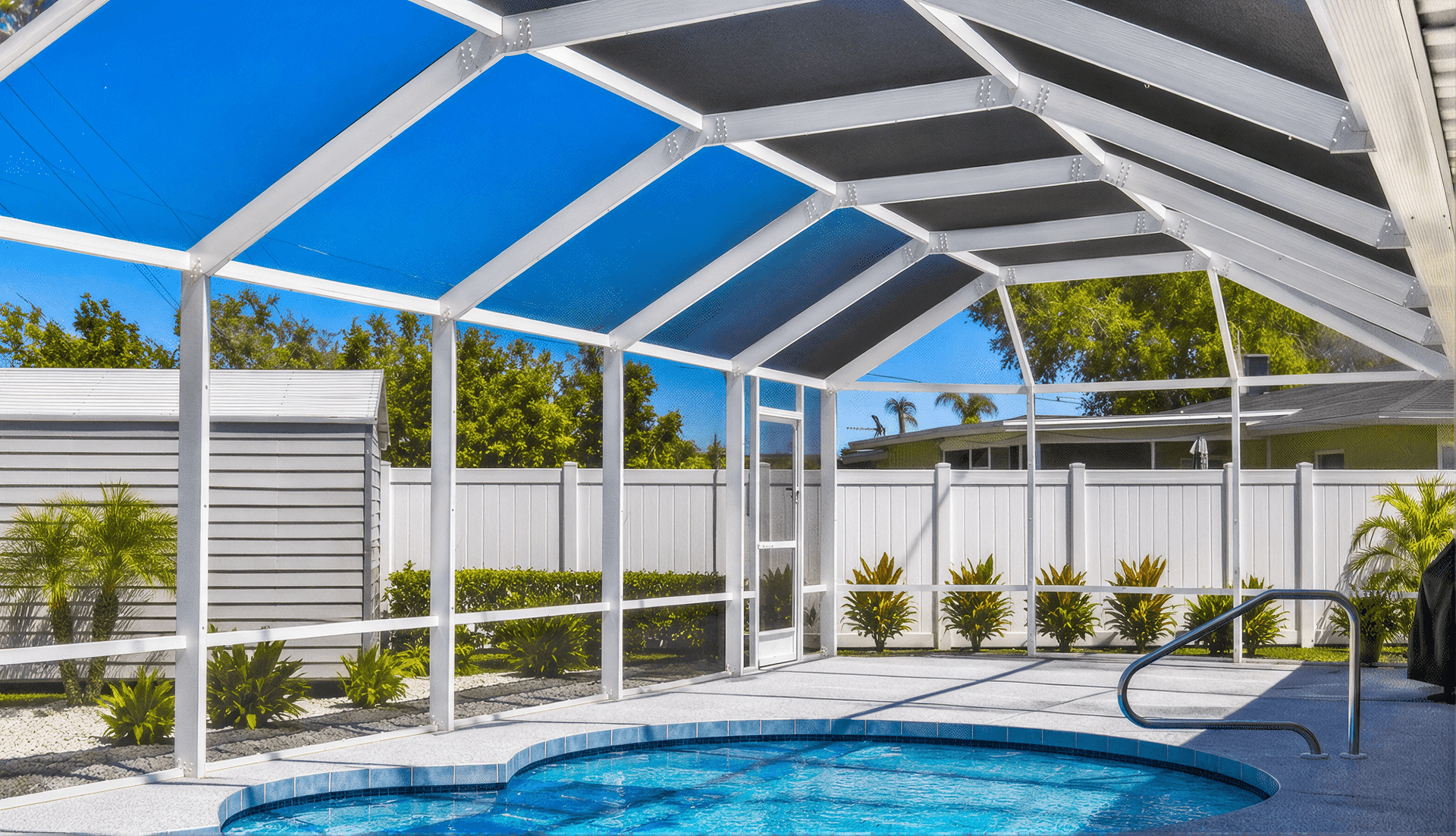 Pool enclosure with retractable white aluminum frame and blue shade panels, featuring a small swimming pool with handrail, white fence, tropical landscaping, and house in background